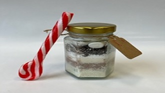 Small glass jar filled, in layers, with hot chocolate ingredients with a candy cane spoon ceside it